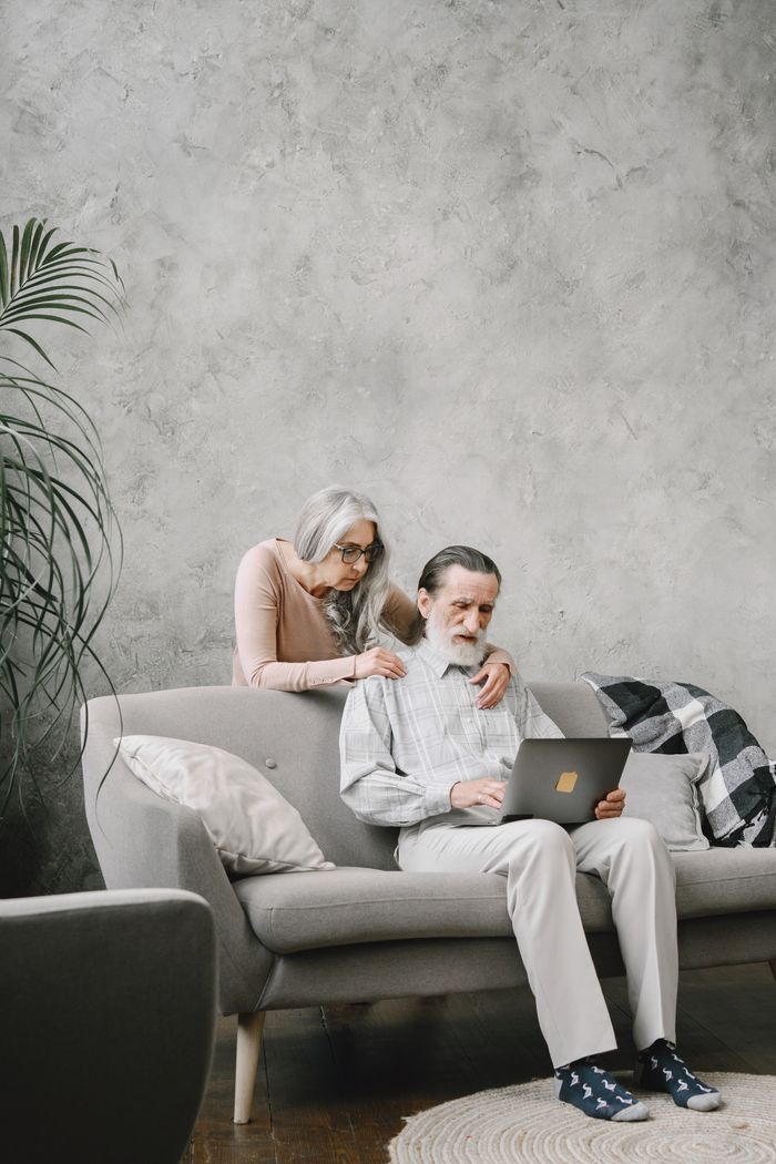 Elderly couple sitting on sofa using laptop, enjoying leisure time together indoors.